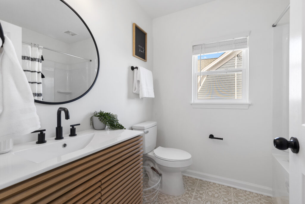 Bathroom with a wood-slat vanity, black fixtures and a round mirror